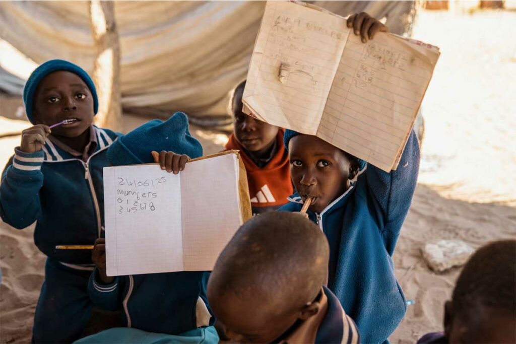Dua bambini con la matita in bocca mostrano gli esercizi sui loro quaderni