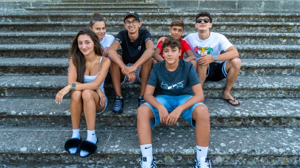 Gruppo di giovani ragazze e ragazzi seduti su una gradinata fissano sorridenti l'obiettivo.