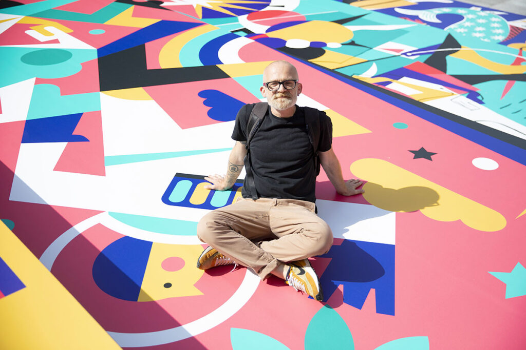 Artista Francesci Poroli seduto su un tappeto colorato creato da lui..