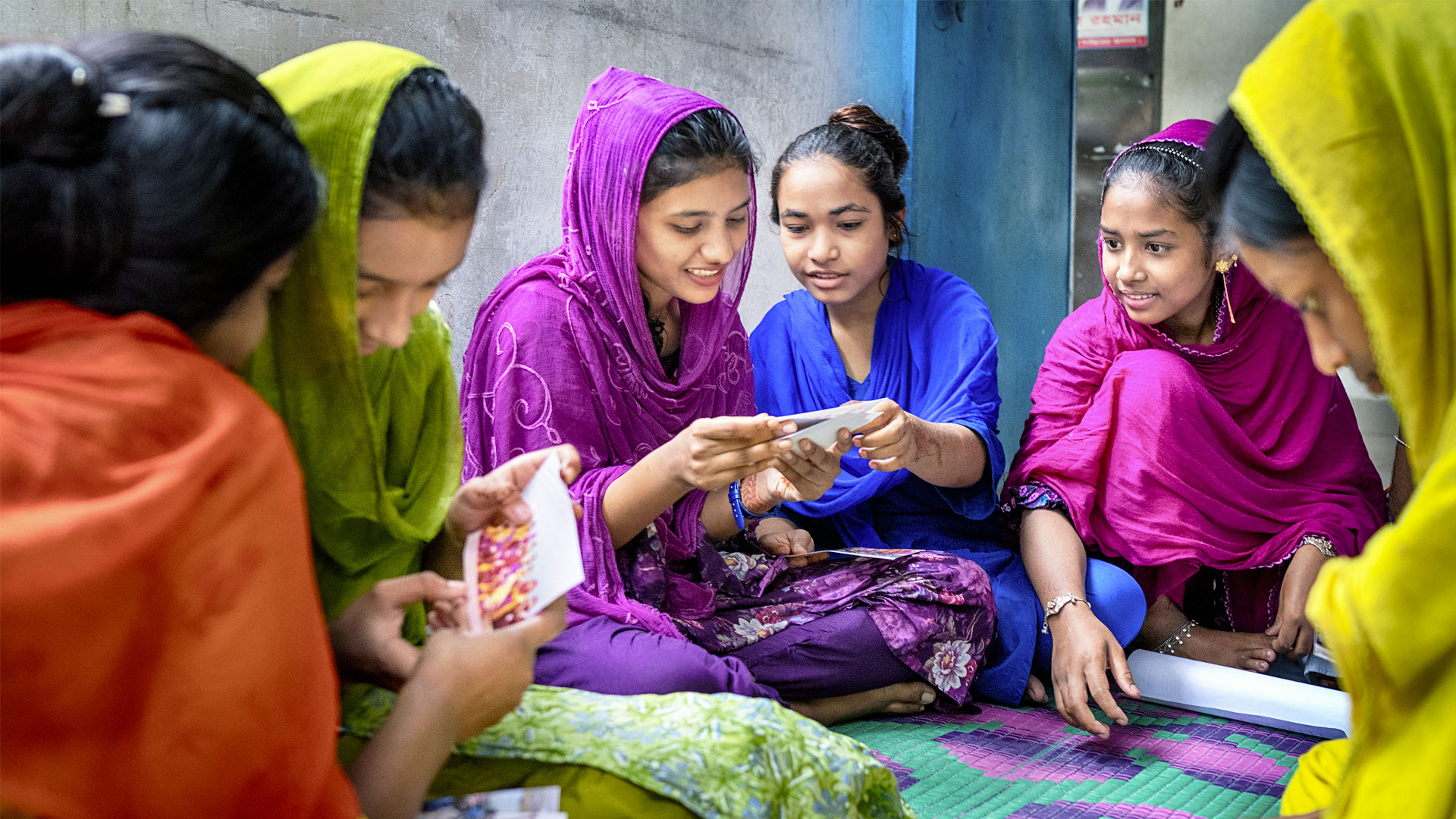 Ragazze in Bangladesh nei loro abiti colorati sorridono sedute in cerchio e guardano fotografie.