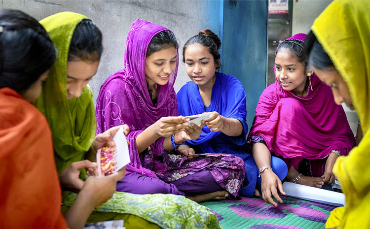 Ragazze in Bangladesh nei loro abiti colorati sorridono sedute in cerchio e guardano fotografie.