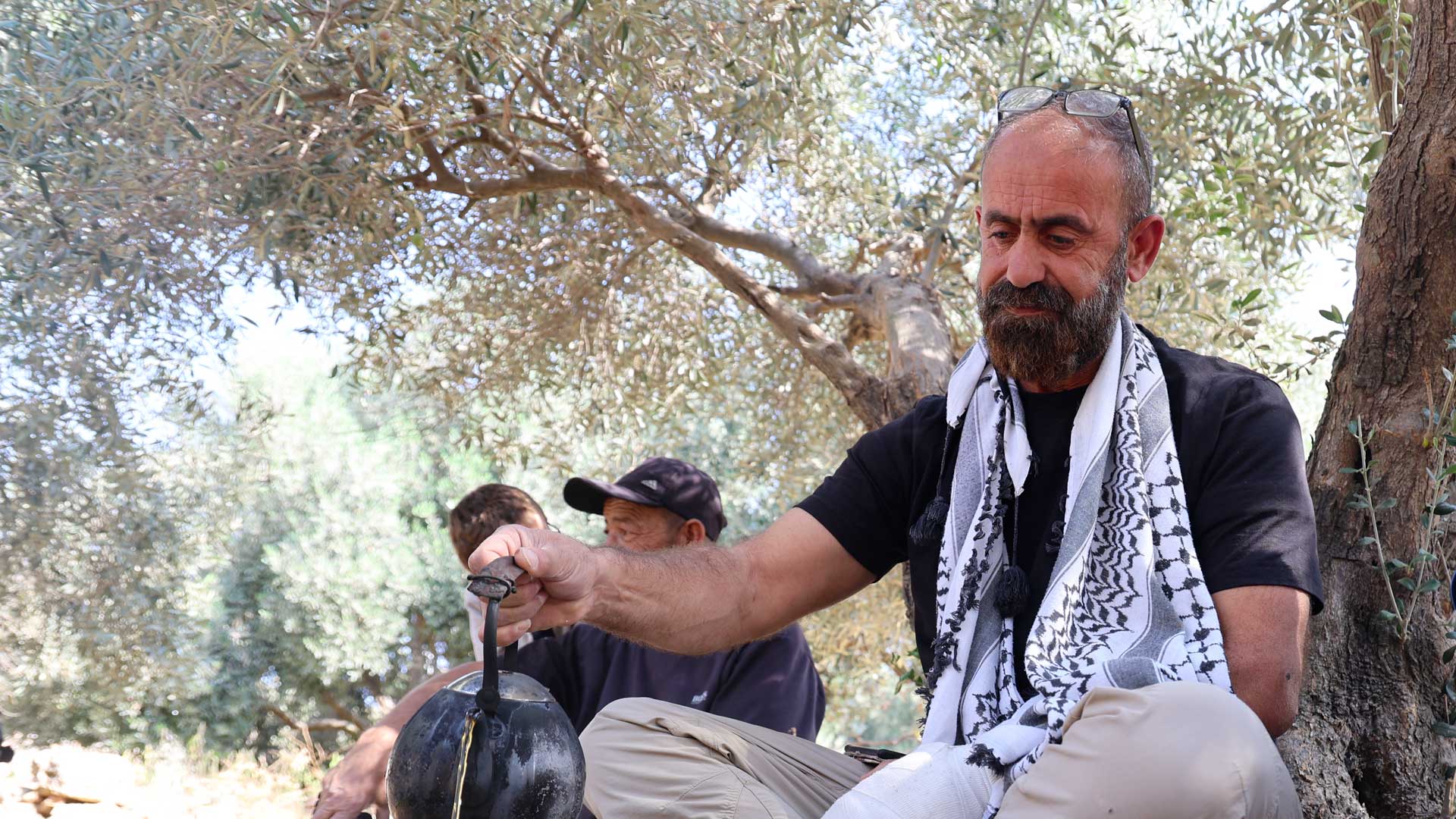 Mahmoud con il braccio sinistro fasciato e legato al collo si versa una tazza di te con la mano destra.