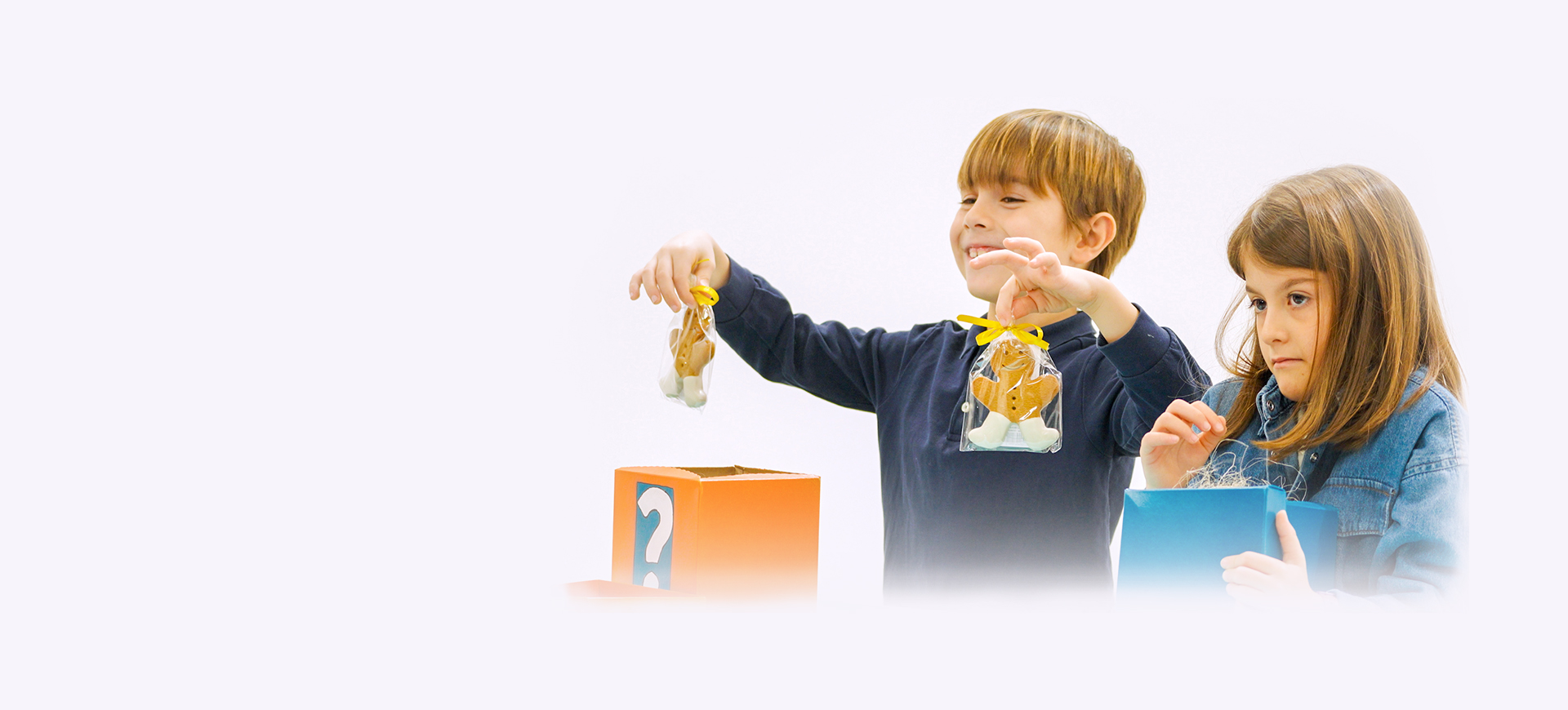 Un bambino felice mostra due confezioni di biscotti natalizi. Vicino a lui una ba,bina triste perché non ha trovato nulla nella scatola.