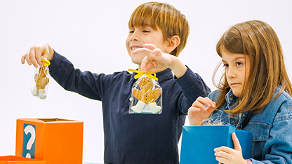 Un bambino felice mostra due confezioni di biscotti natalizi. Vicino a lui una ba,bina triste perché non ha trovato nulla nella scatola.