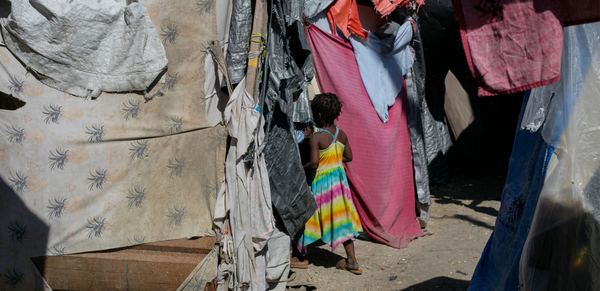 Una bambina entra in una tenda ottenuta con tessuti vari e stracci.