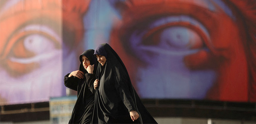 Due donne iraniane con il velo camminano davanti a un murales