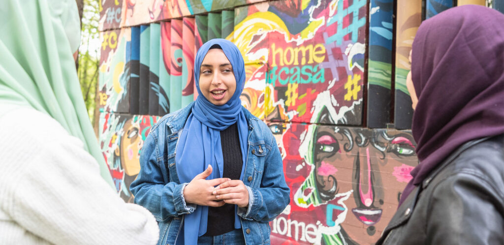 Ragazza con il velo davanti a un murlaes parla con due amiche.