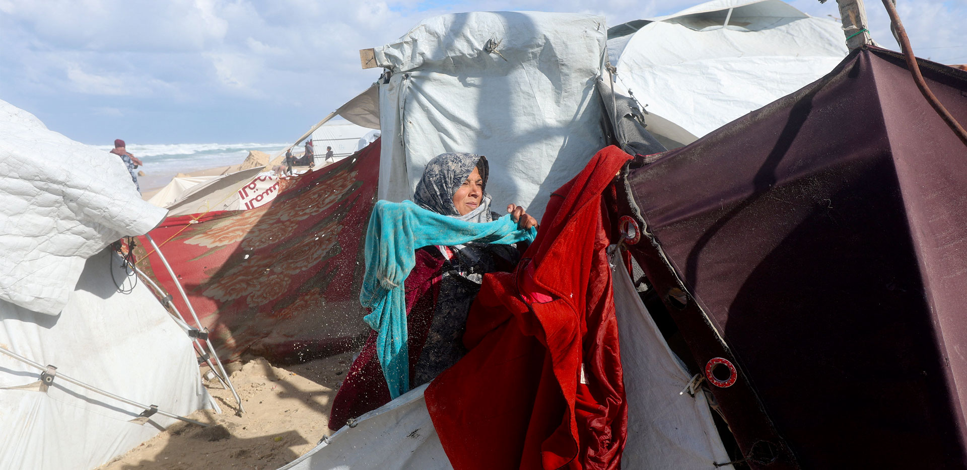 Una donna palestinese fuori dalle tende di emergenza guarda il cielo pensierosa.