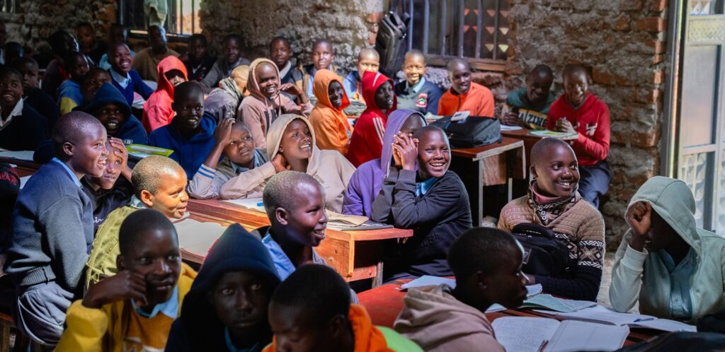 Un gruppo di bambine ugandesi sorridenti e felici sono in una classe seduti ai banchi