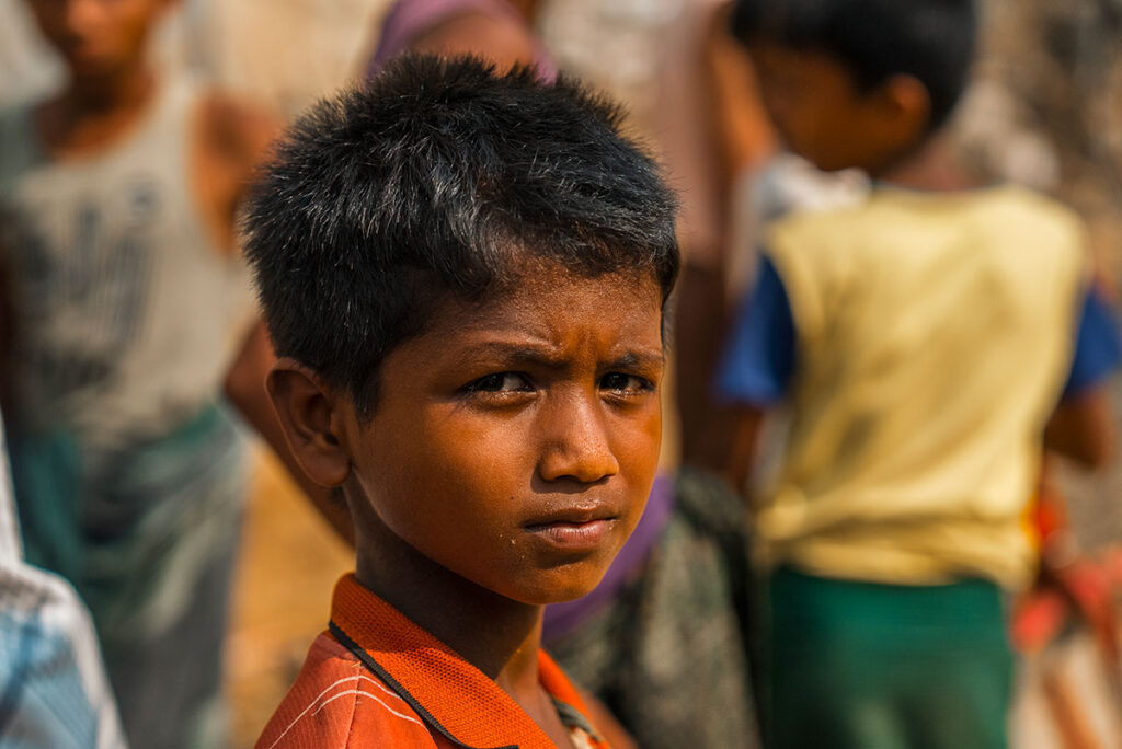 Viso in primo piano di un bambino Rohingya, che vive in un campo profughi di Cox's Bazar. Il suo sguardo fissa l'obiettivo. È triste e inteso.
