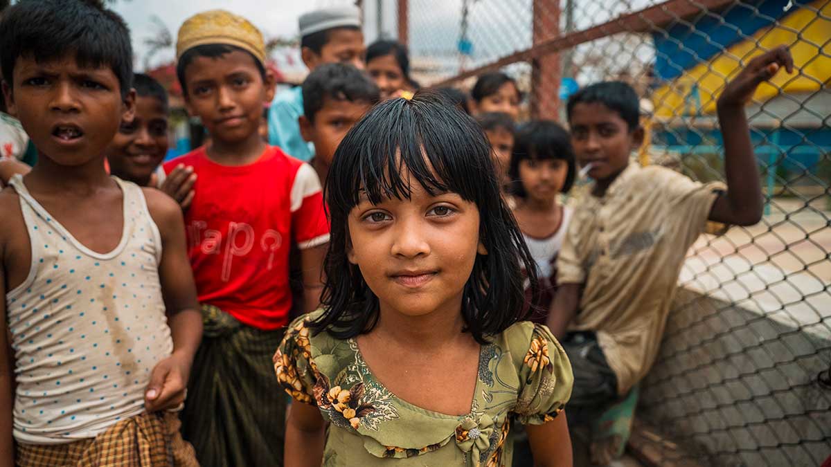 Il primo piano di una bambina del Cox's Bazar, sullo sfondo si vedono altri bambini che guardano verso l'obiettivo.