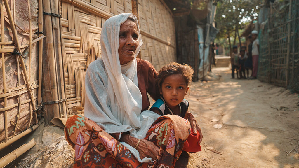 Una signora anziana Rohingya, seduta in terra, tiene in braccio un bambino. Si trova nel campo profughi di Cox's Bazar, in Bangladesh.