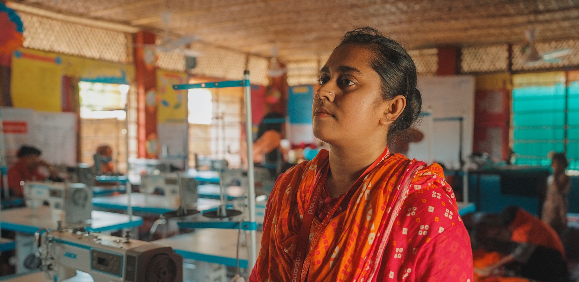 Farzana in primo piano, fa parte dello staff di ActionAid Bangladesh e lavora in uno degli spazi sicuri per donne e ragazze a Cox’s Bazar. Nello sfondo si intravedono postazioni con macchine da cucire.
