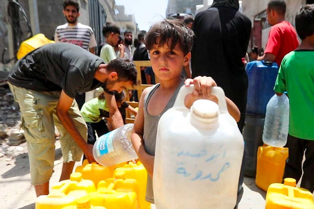 Un bambino palestinese tiene in mano una tanica in fila per rifornimento di acqua insieme ad altri bambini e adulti
