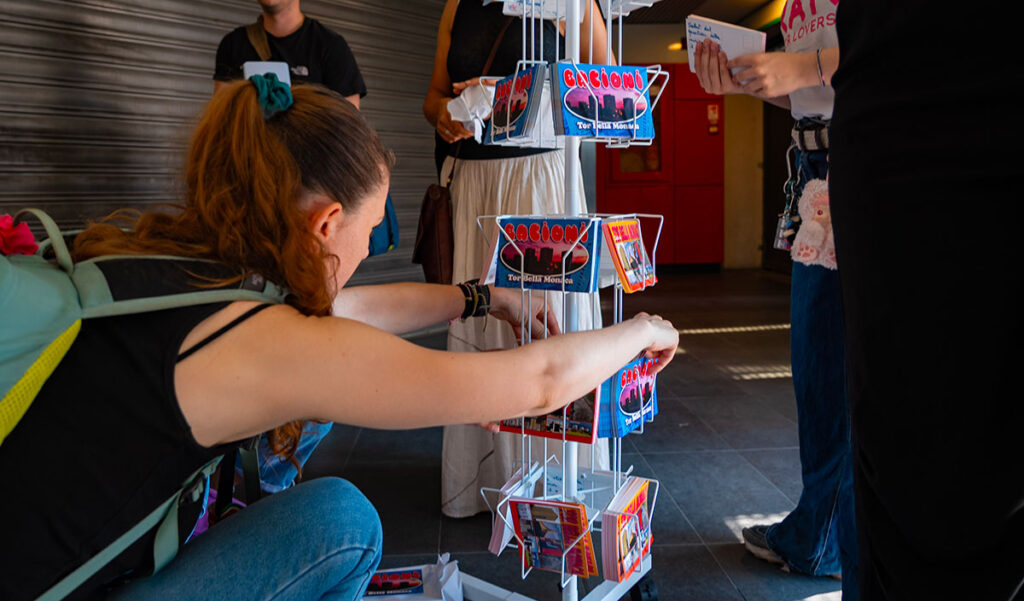 Una studentessa è accovacciata davanti a un totem e sta sistemando le cartoline di Tor Bella Moniaca pronte per la vendita.
