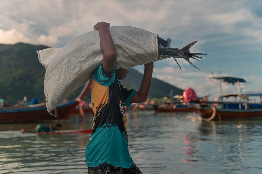Una donna thailandese trasporta sulle spalleun sacco contenente del pesce.