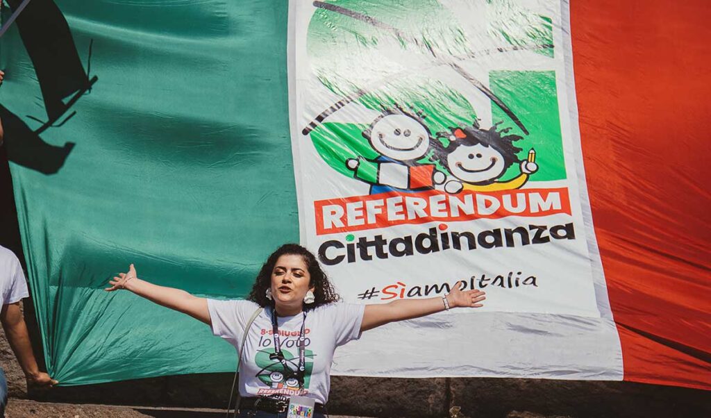 Una donna apre le braccia in segno di vittoria davanti alla bandiera di cittadinanza attiva per il referendum