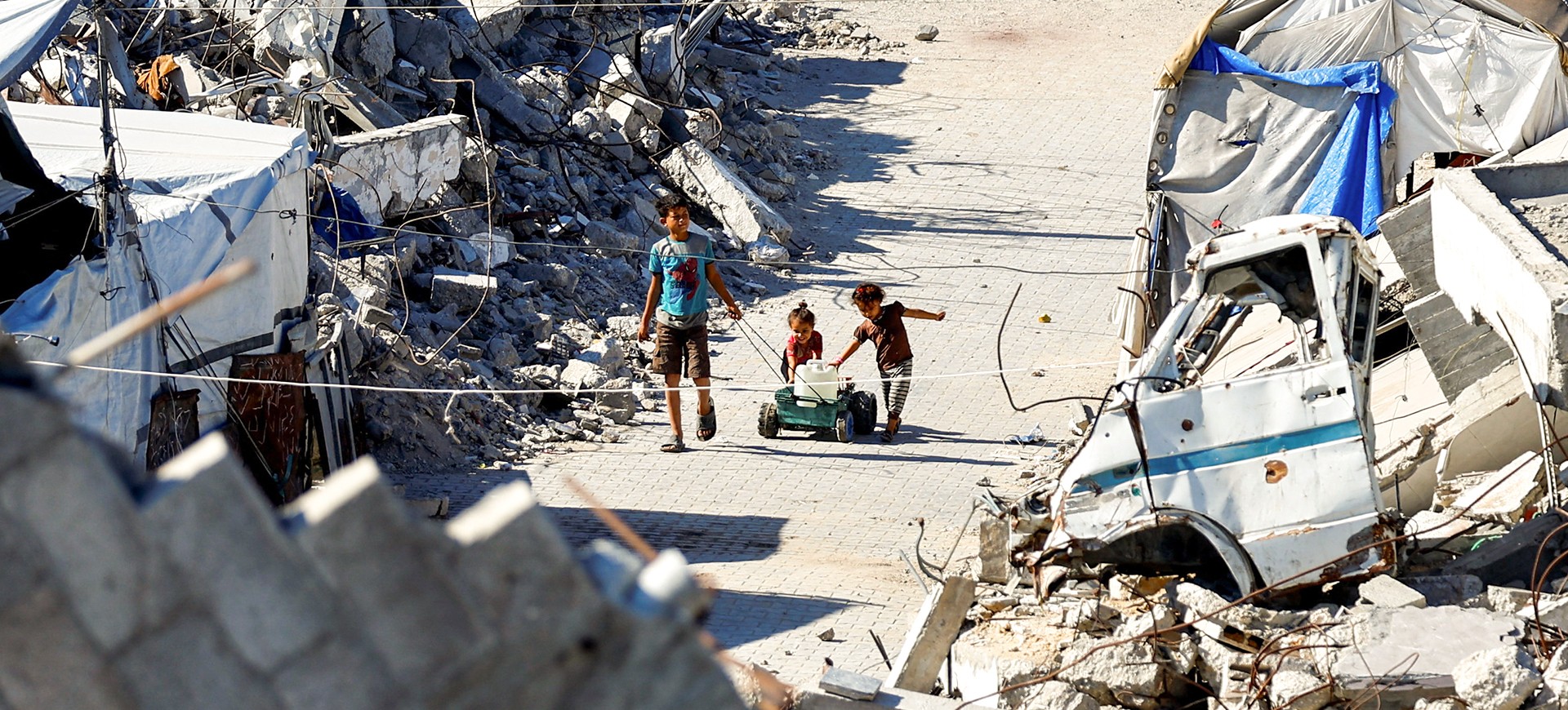 Tre bambini palestinesi di circa 10-7 e 2 anni giocano in mezzo alle macerie.