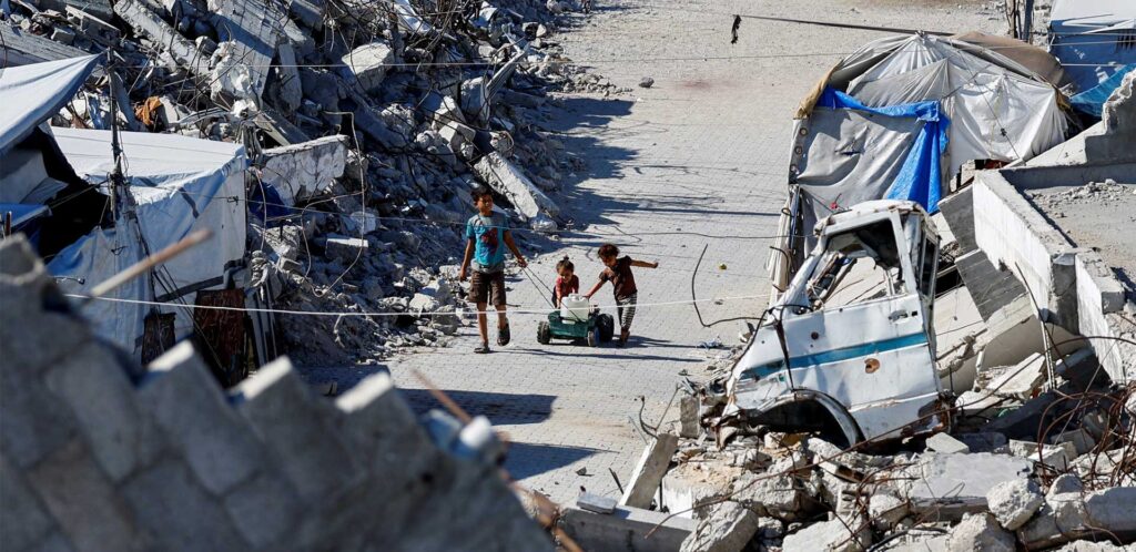 Tre bambini palestinesi di circa 10-7 e 2 anni giocano in mezzo alle macerie.