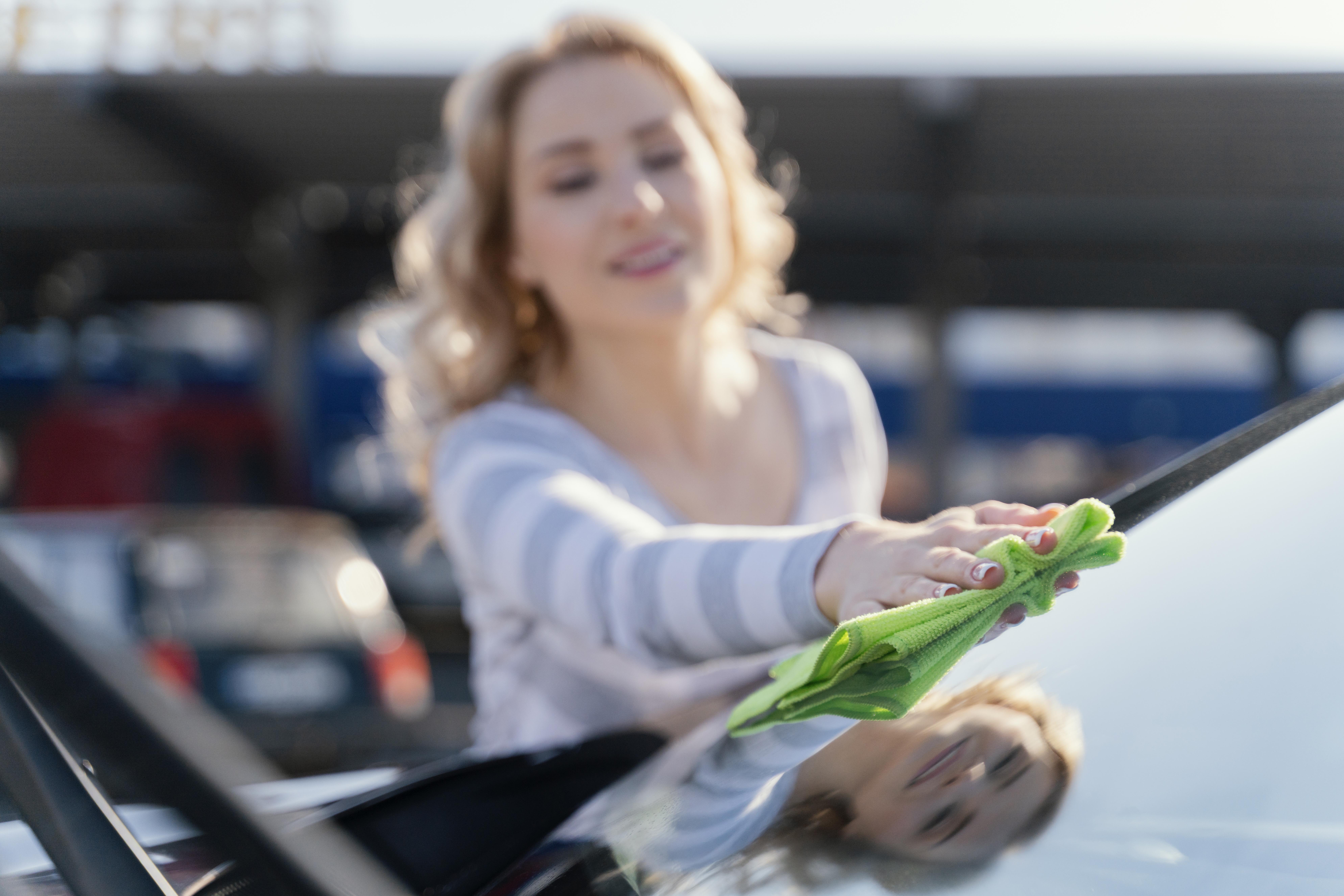 Henkilö pesee autoa painepesurilla ja pesukintaalla aurinkoisella kotipihalla.