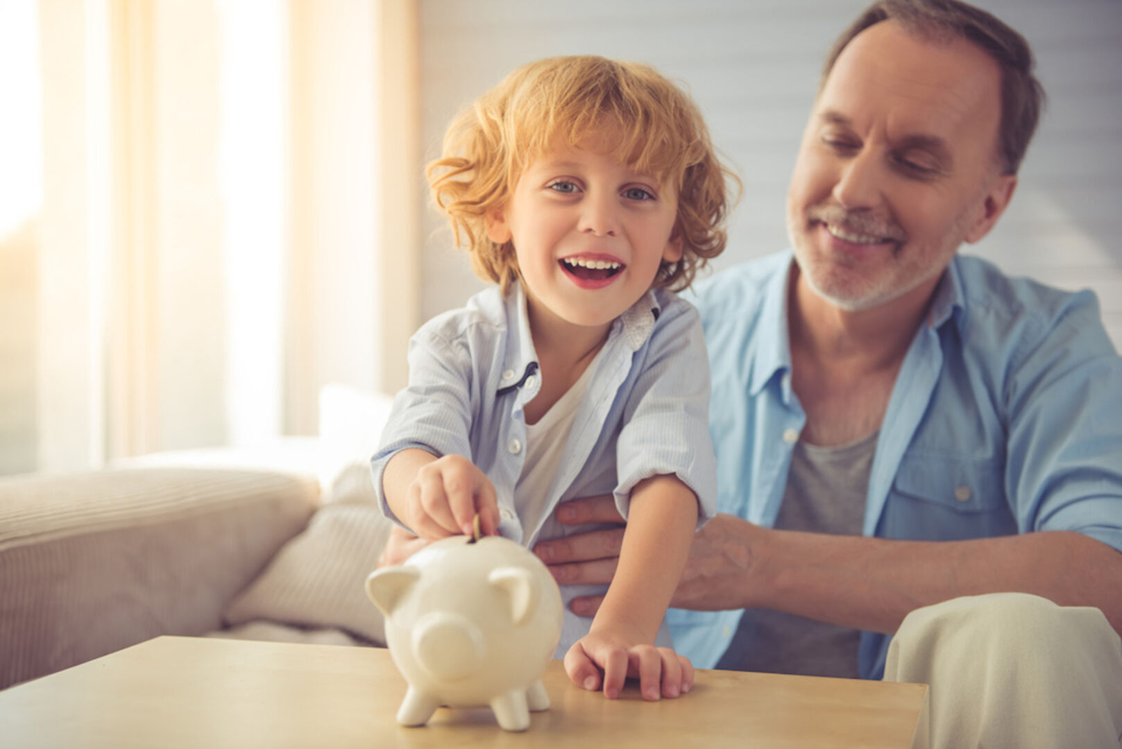 Ein Kind wirft Geld in ein Sparschwein, Vater wirkt zufrieden.