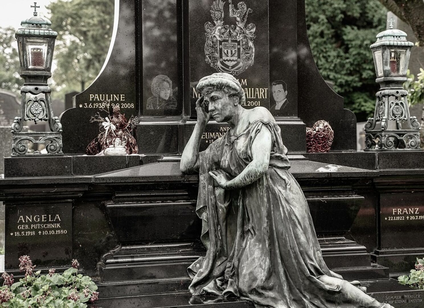 Statue einer trauernden Frau vor schwarzen Grabsteinen