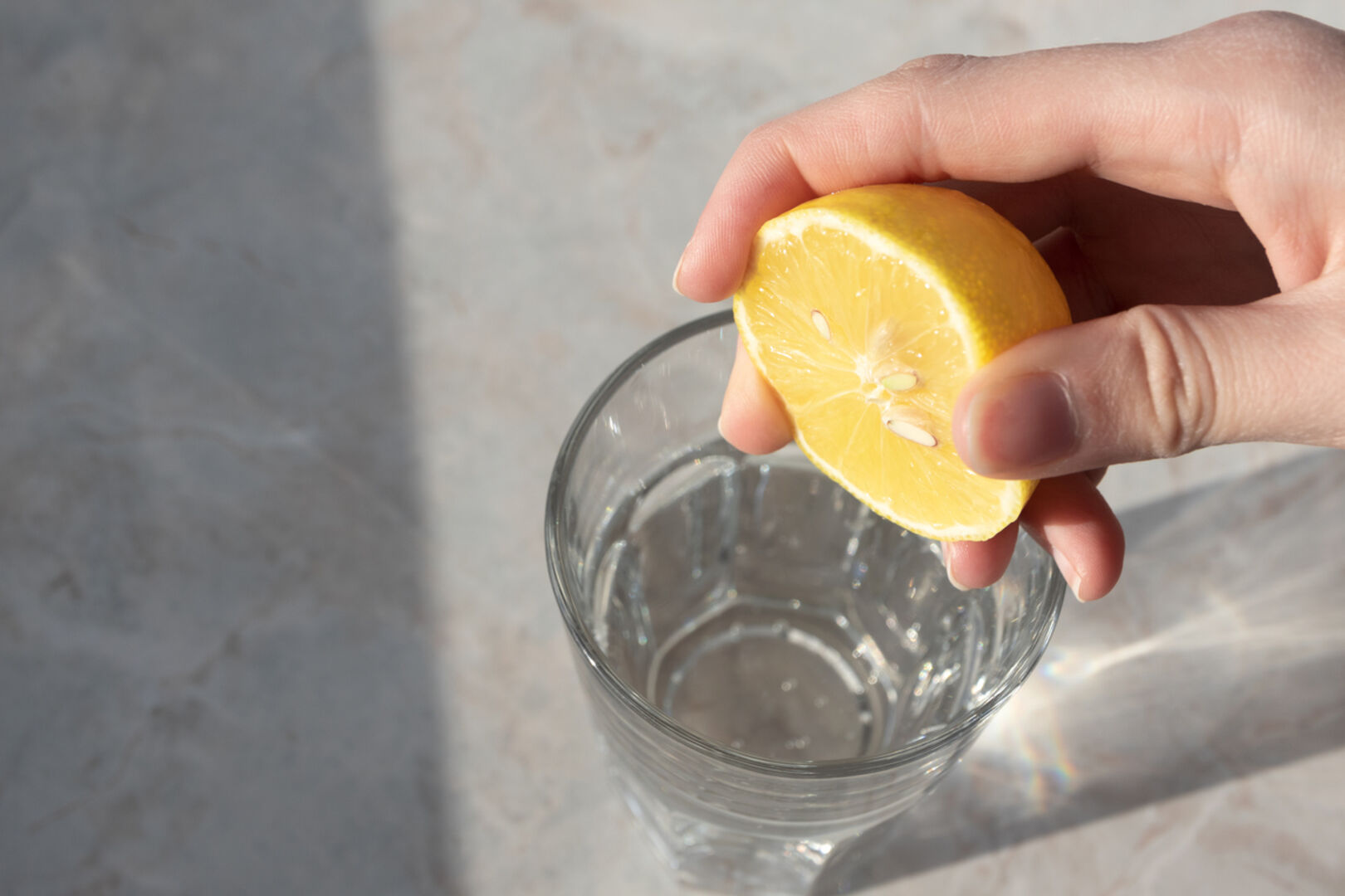 Eine Frau presst eine halbe Zitrone in ein Glas Wasser.