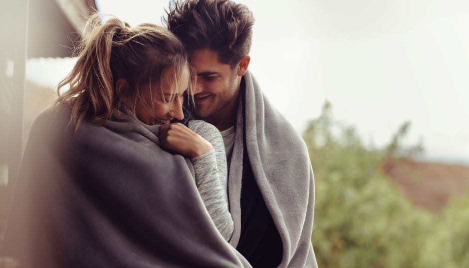 Verliebtes Paar wärmt sich unter einer gemeinsamen Decke gegen die Kälte | Credit: iStock.com/jacoblund