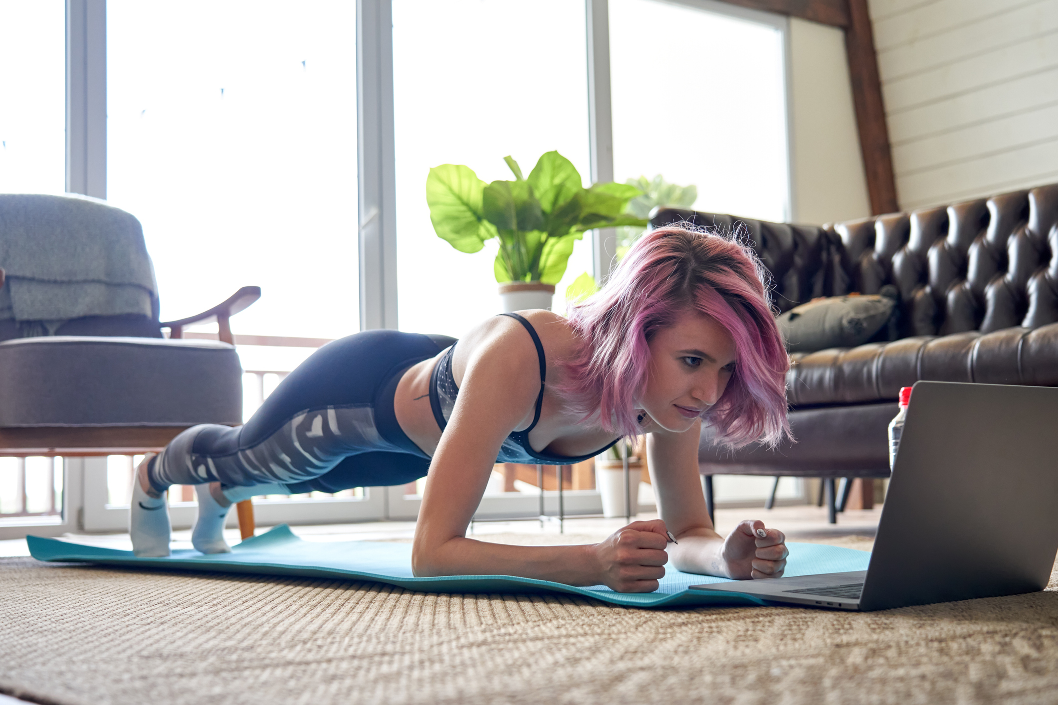 Junge Frau bei Fitnessübungen vor dem Laptop im Wohnzimmer