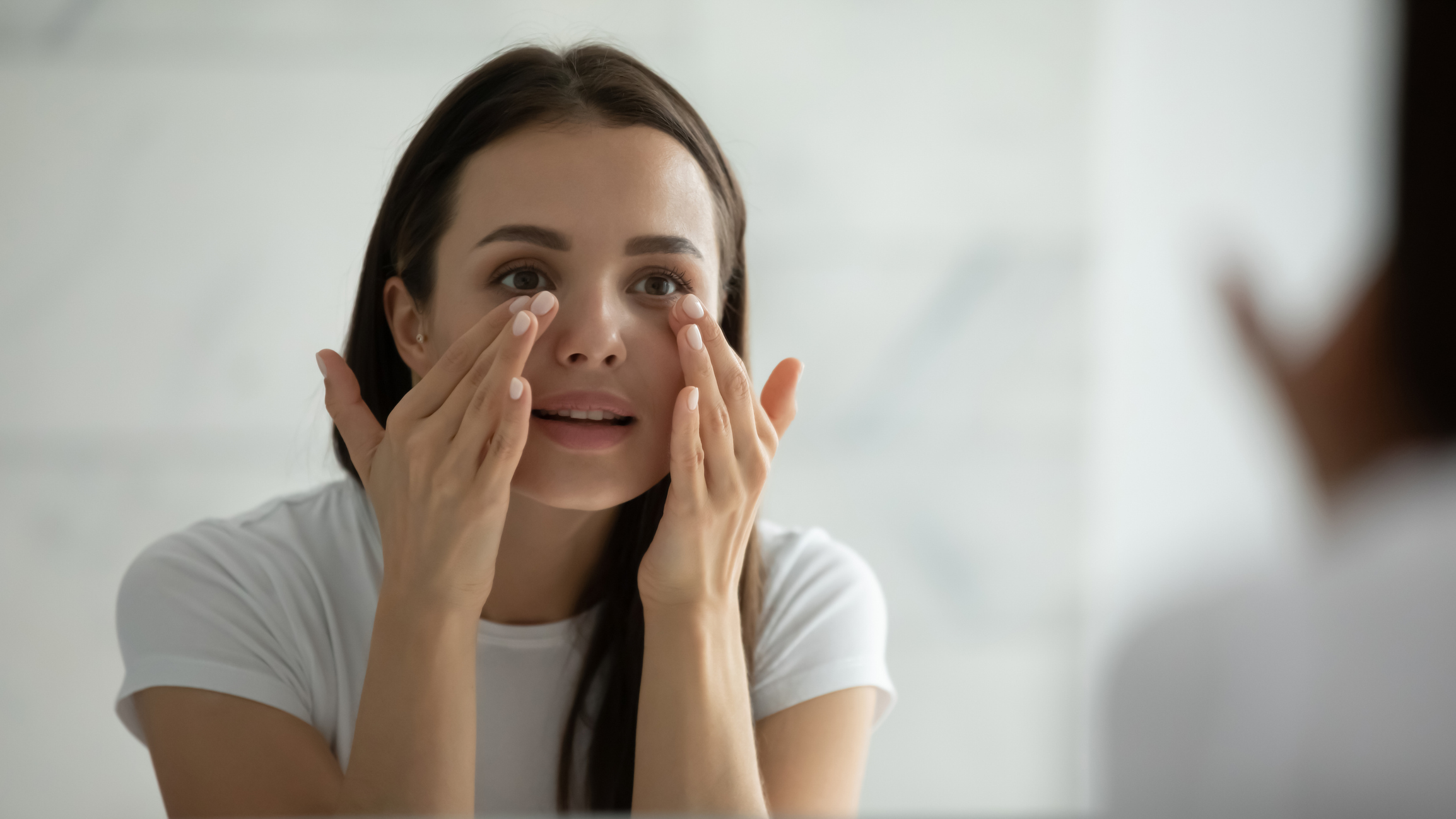 Spiegelbild einer jungen Frau, die Gesichtscreme aufträgt