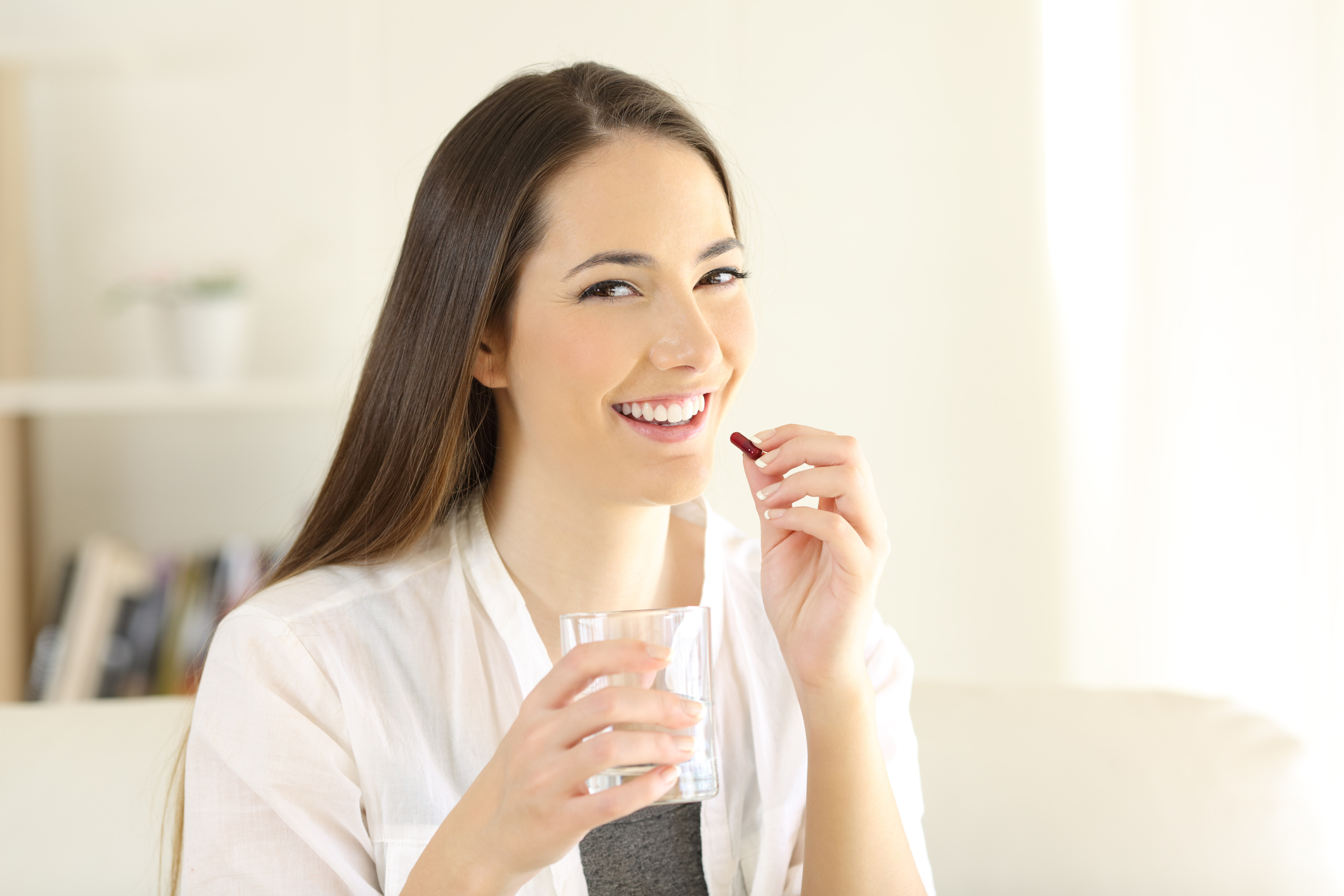 Junge Frau mit einem Glas Wasser in der einen und einer Medikamentenkapsel in der anderen Hand