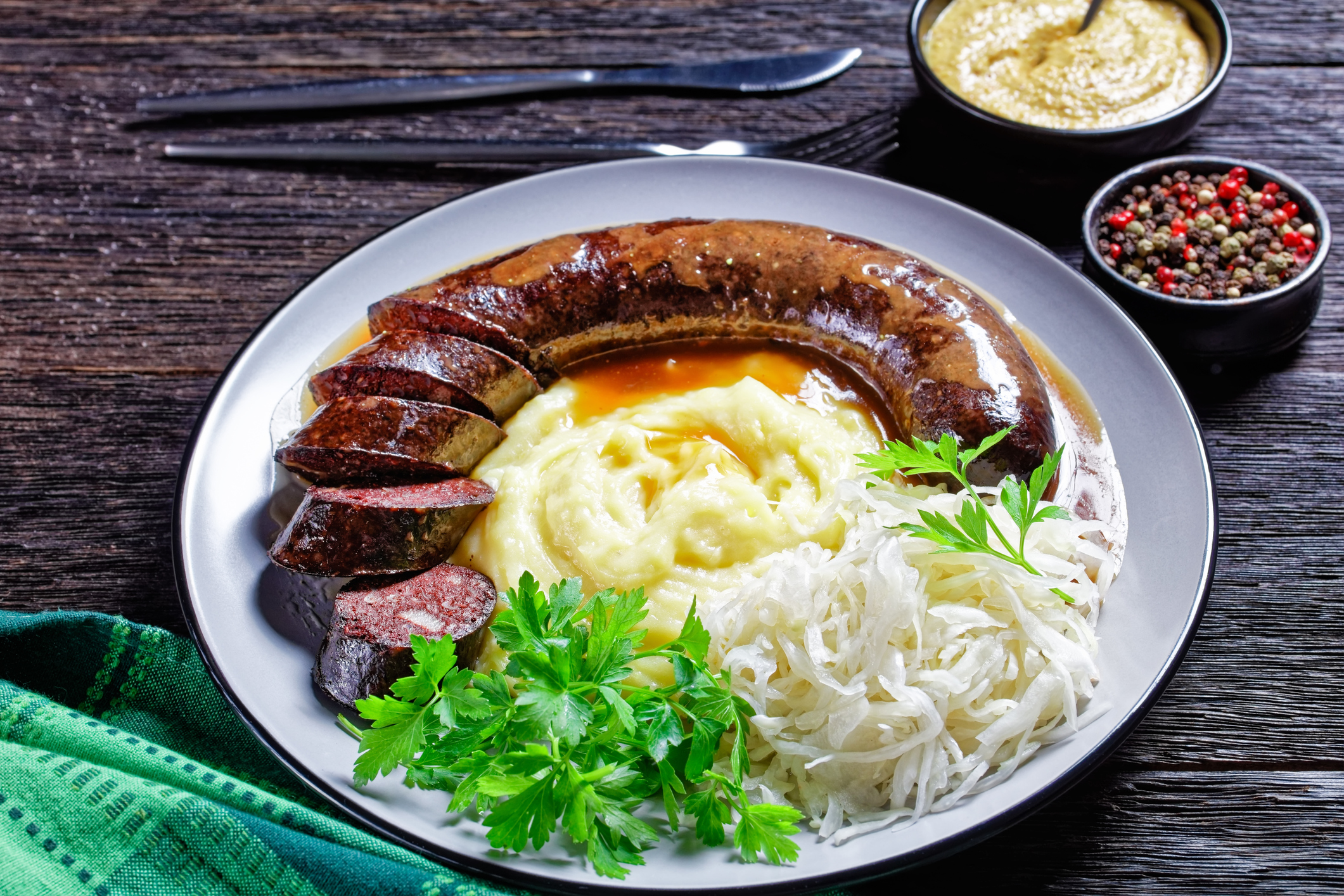Eine gebratene Blutwurst mit Kartoffelpüree und Sauerkraut auf einem Teller mit Salatgarnierung