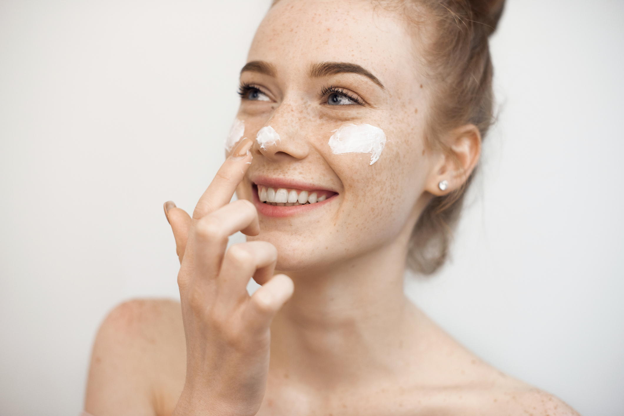 Junge Frau mit Sommersprossen tupft sich Creme ins Gesicht