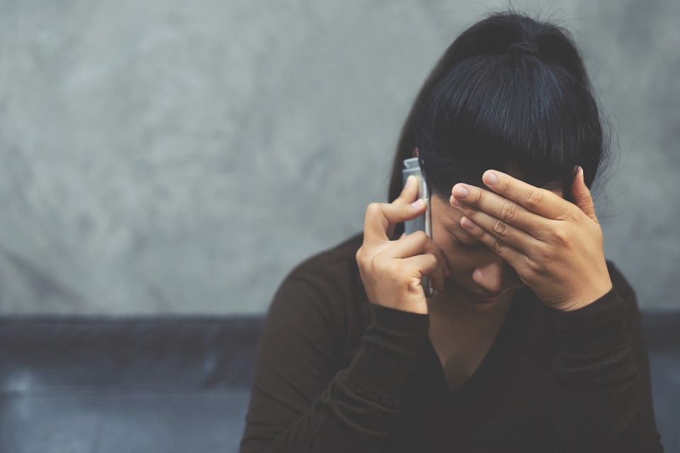 Eine dunkelhaarige Frau telefoniert. Sie blickt zu Boden und hat die Hand an die Stirn gelegt.
