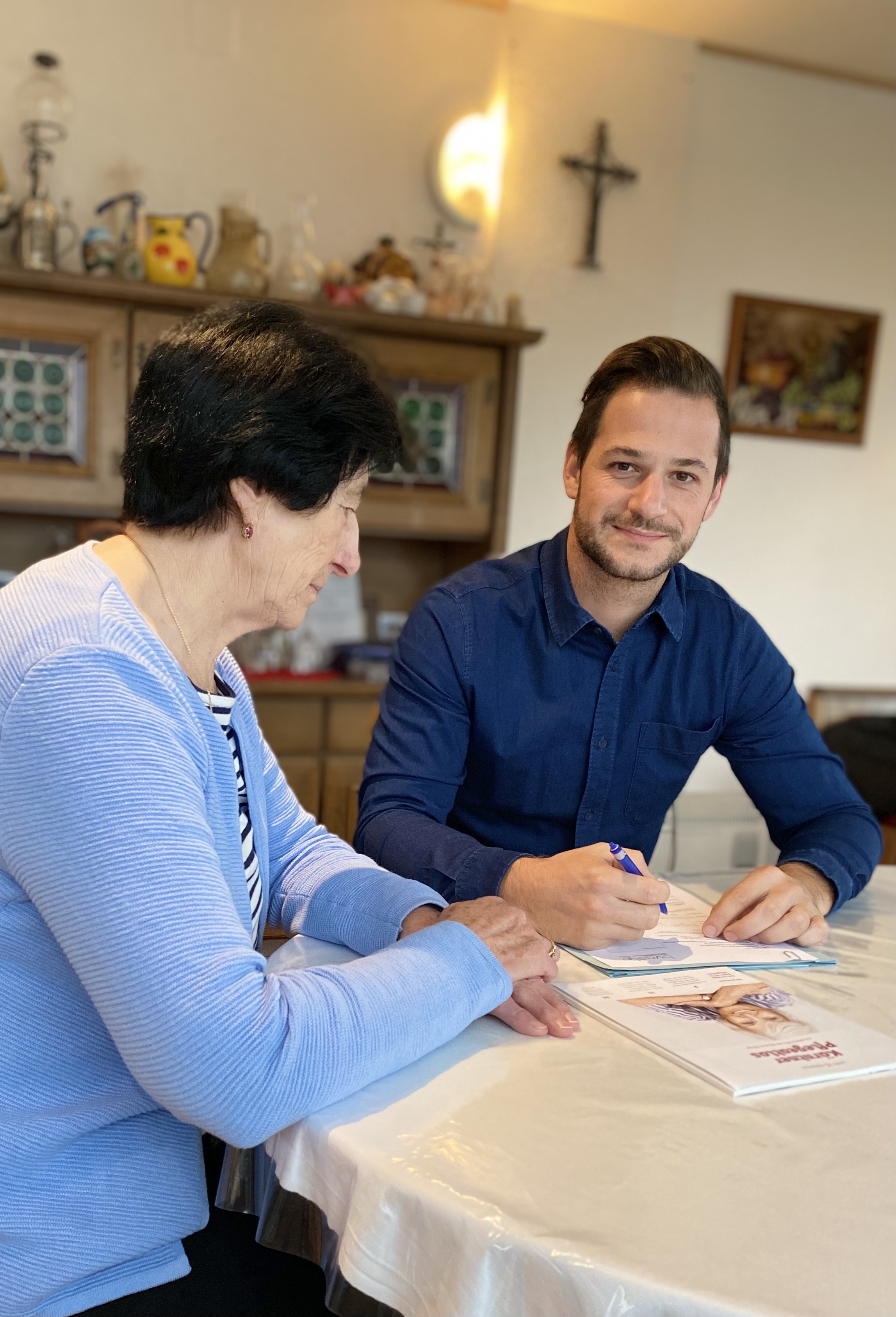 Pflegekoordinator Markus Pernull berät eine ältere Dame in ihrem Wohnzimmer