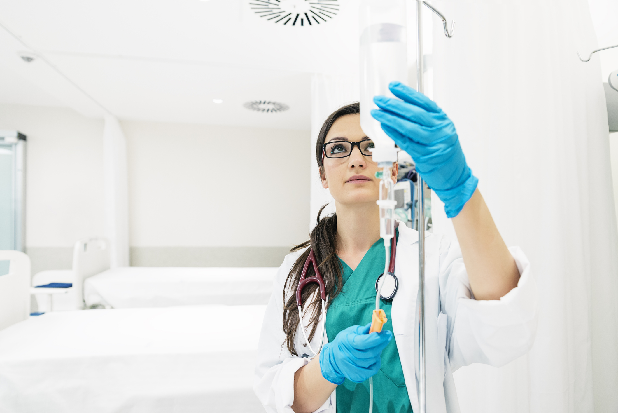Eine junge Krankenschwester mit langen braunen Haaren und Brille bereitet eine Infusion vor