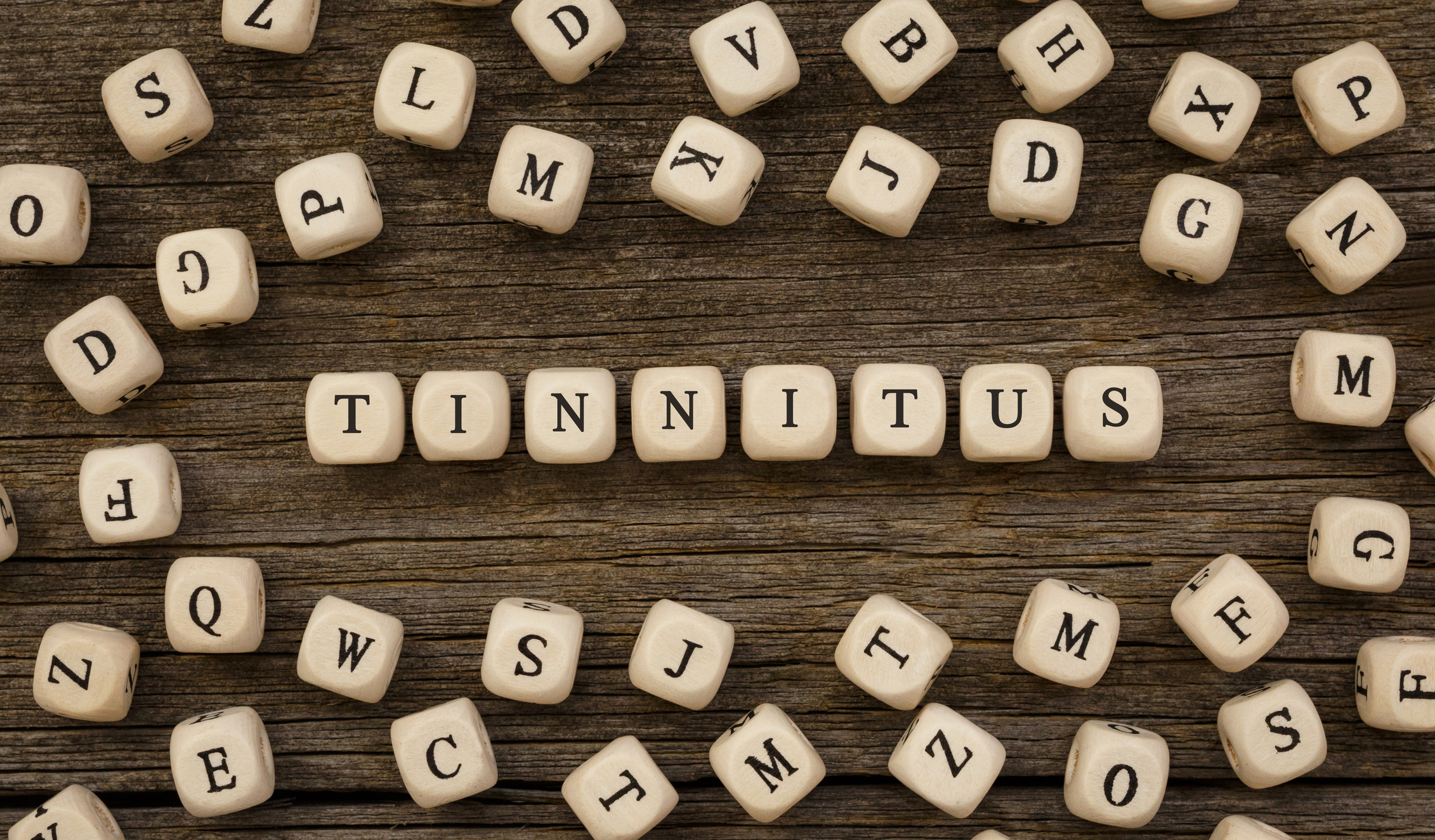 Mehrere Buchstabenwürfel bilden auf einem Holztisch das Wort Tinnitus