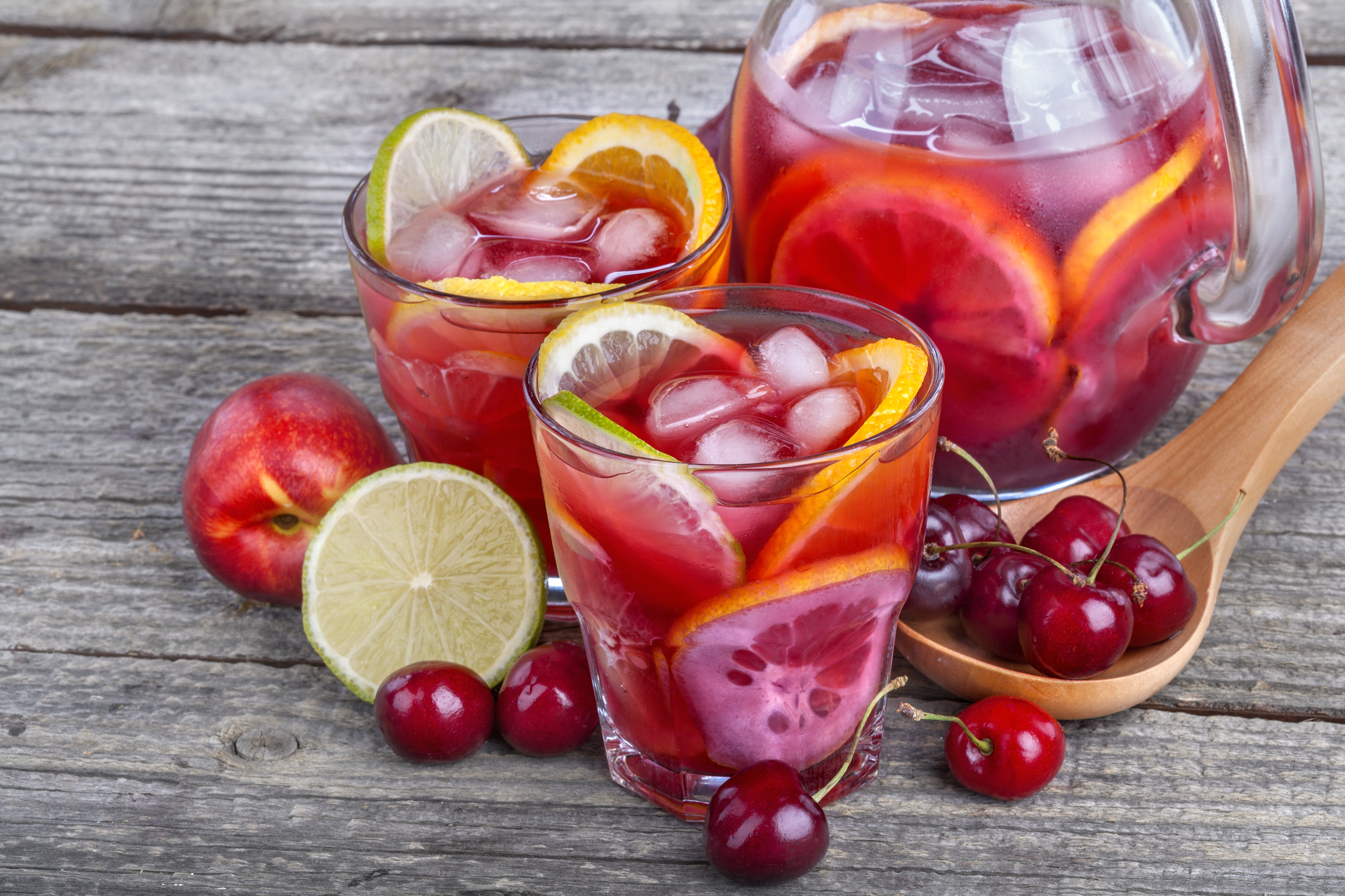 2 Gläser mit Orangenschalen, Limettenschalen, Kirschen und Eiswürfel
