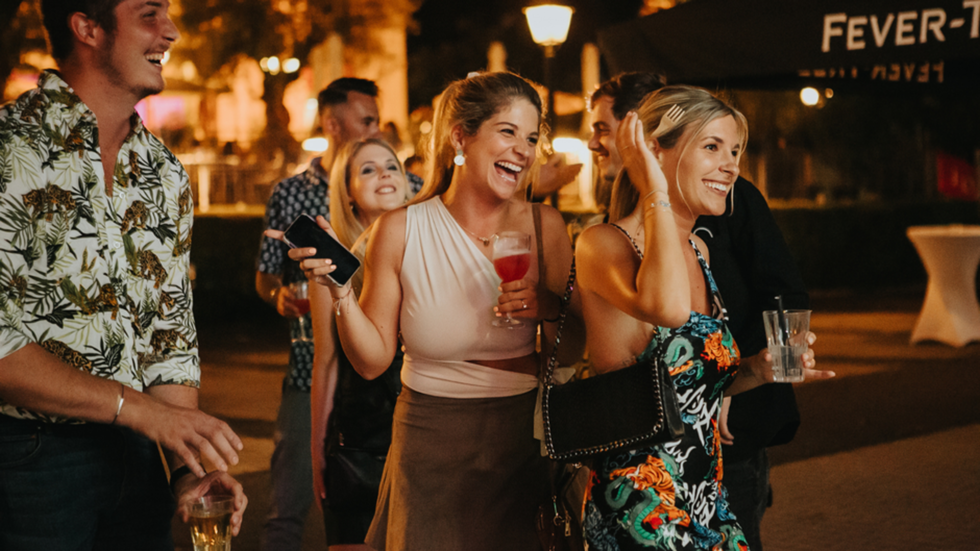 Nacht, zwei Frauen die lachen und Drinks in der Hand halten.