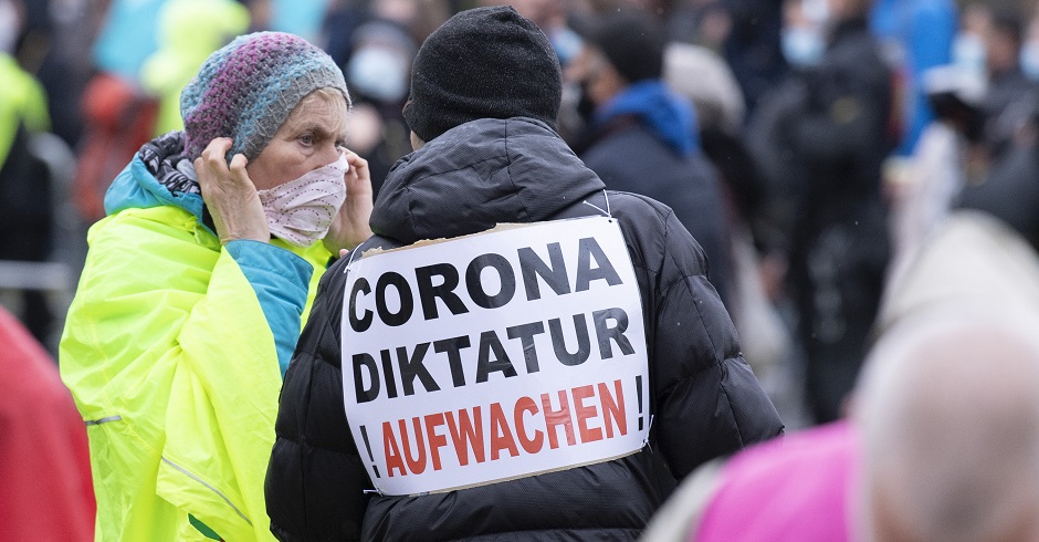 Ein Mann trägt ein Schild auf dem Rücken. Darauf steht: "Corona Diktatur ! Aufwachen !"