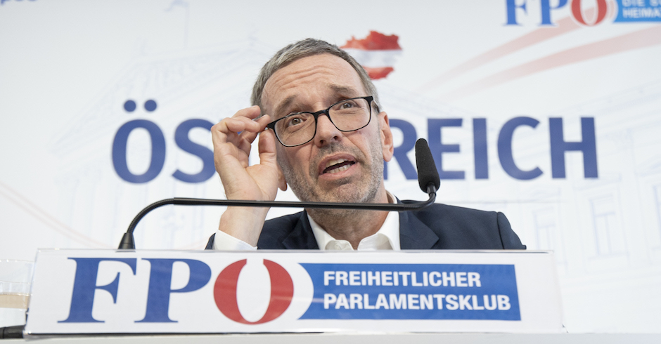 Herbert Kickl auf einer Pressekonferenz im Portrait. Hinter ihm der Schriftzug "Österreich". Unter seinem Mikrofon ein Aufsteller mit dem Logo der FPÖ und dem Text: "Freiheitlicher Parlamentsklub"
