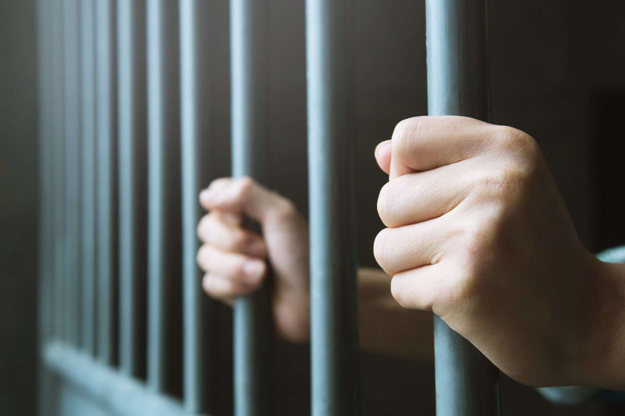Zwei Hände, die zwei Gitterstäbe einer Gefängnistür umschließen