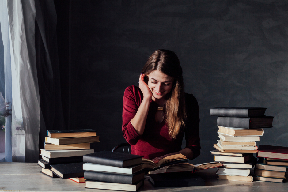 Gut gelaunte Studentin sitzt über ihren Büchern und lernt | Credit: iStock.com/DmitriiSimakov
