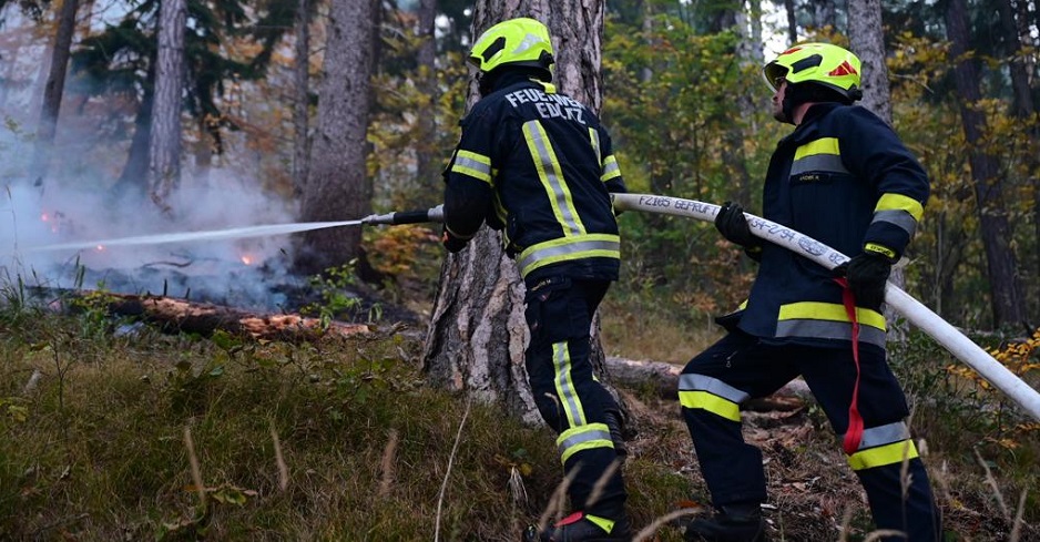 Zwei Feuerwehrmänner löschen einen Glutherd im Wald.