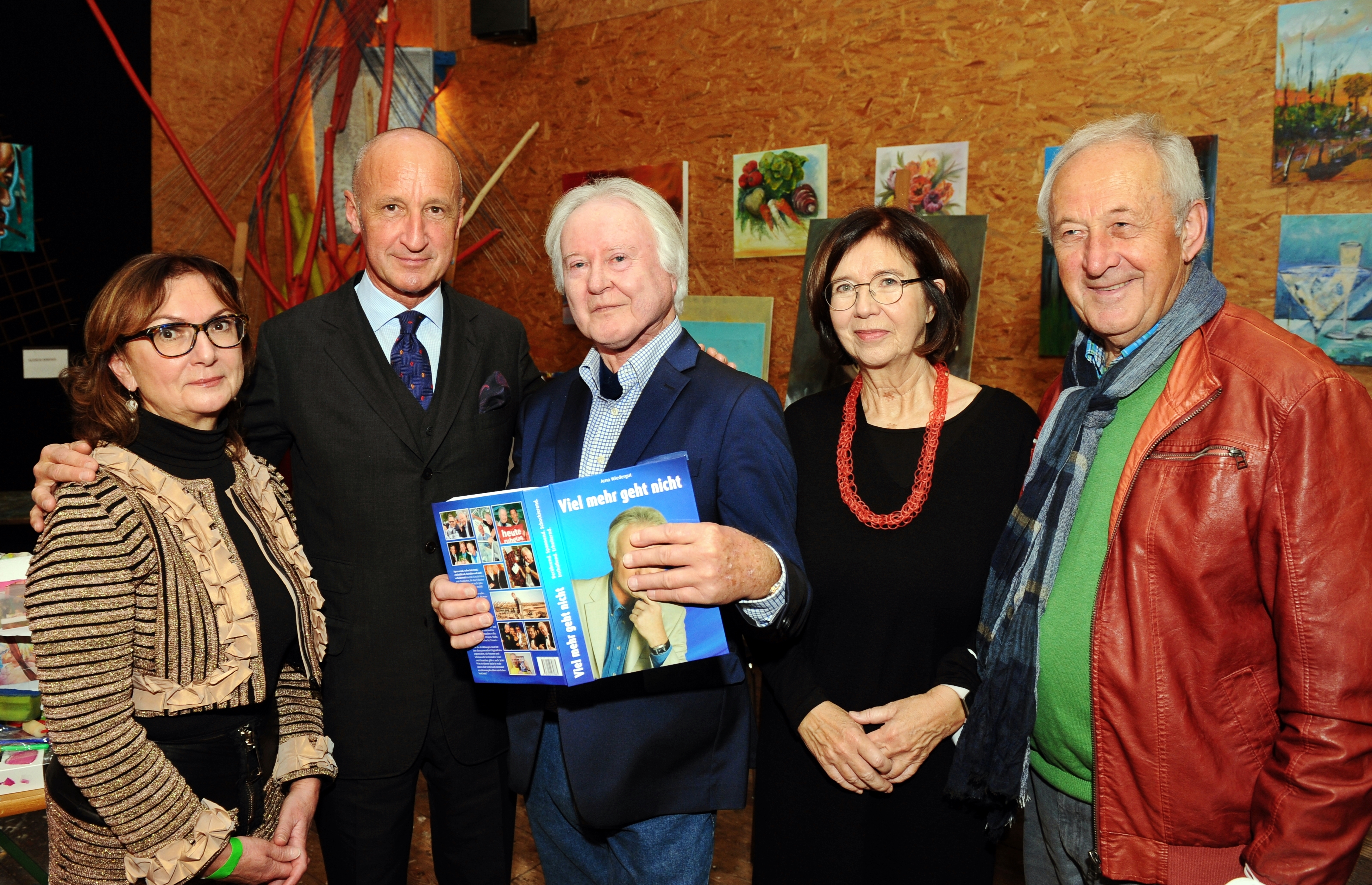 Arno Wiedergut steht mit seinem Buch in der Hand inmitten von Besuchern seiner Buchpräsentation