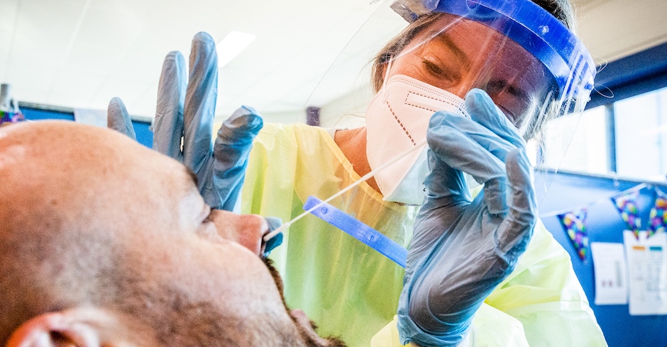 Eine Frau mit Gesichts-Schild entnimmt mit Stäbchen Probe aus der Nase von Mann