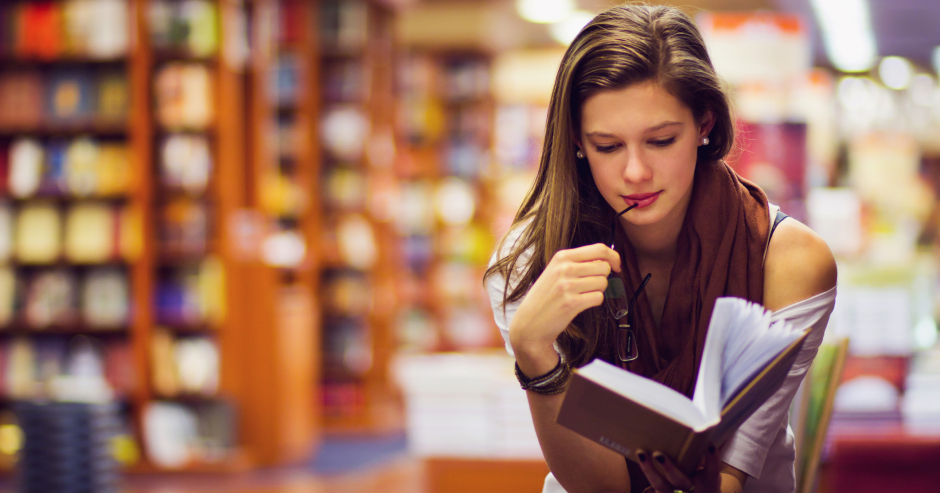 Junge Frau, vertieft in ihr Buch, in einer Buchhandlung | Credit: iStock.com/orbandomonkos