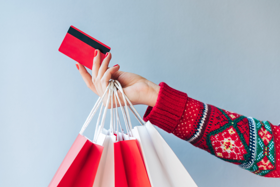 Frau mit weihnachtlichen Einkaufstaschen in der seitlich ausgestreckten Hand | Credit: iStock.com/Wpadington