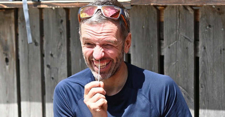 Herbert Kickl macht einen Corona-Selbstest. Er fährt mit einem Wattestäbchen in die Nase und zieht eine Grimasse. Kickl trägt eine Sonnenbrille am Kopf und sitzt vor einer Holzwand. Das Foto ist bei einer Wanderung entstanden.