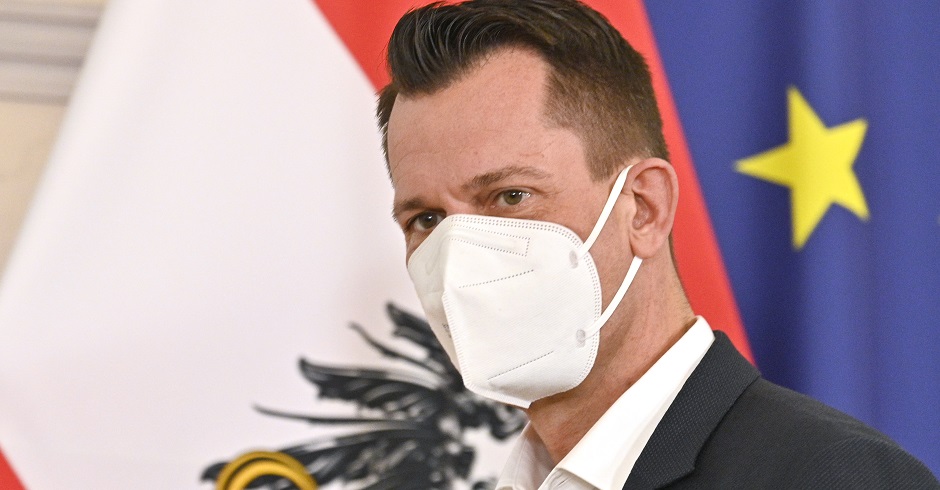 Gesundheitsminister Wolfgang Mückstein mit FFP-2 Maske vor der europäischen und österreichischen Flagge.